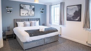 Een slaapkamer met een bed, nachtkastjes, een raam met gordijnen en wanddecoratie.