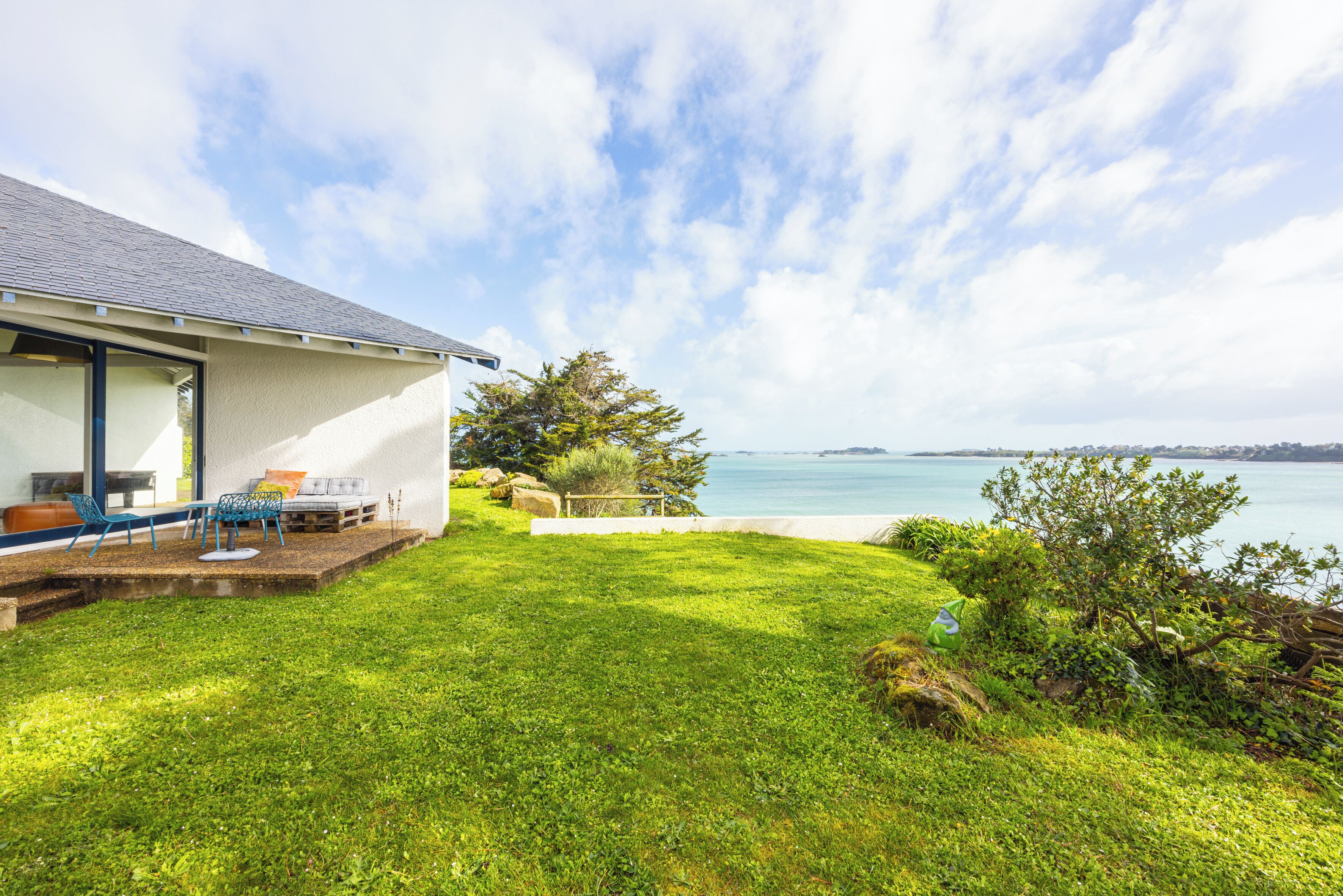 Una casa moderna con jardín, un patio amueblado al aire libre y vistas al mar.