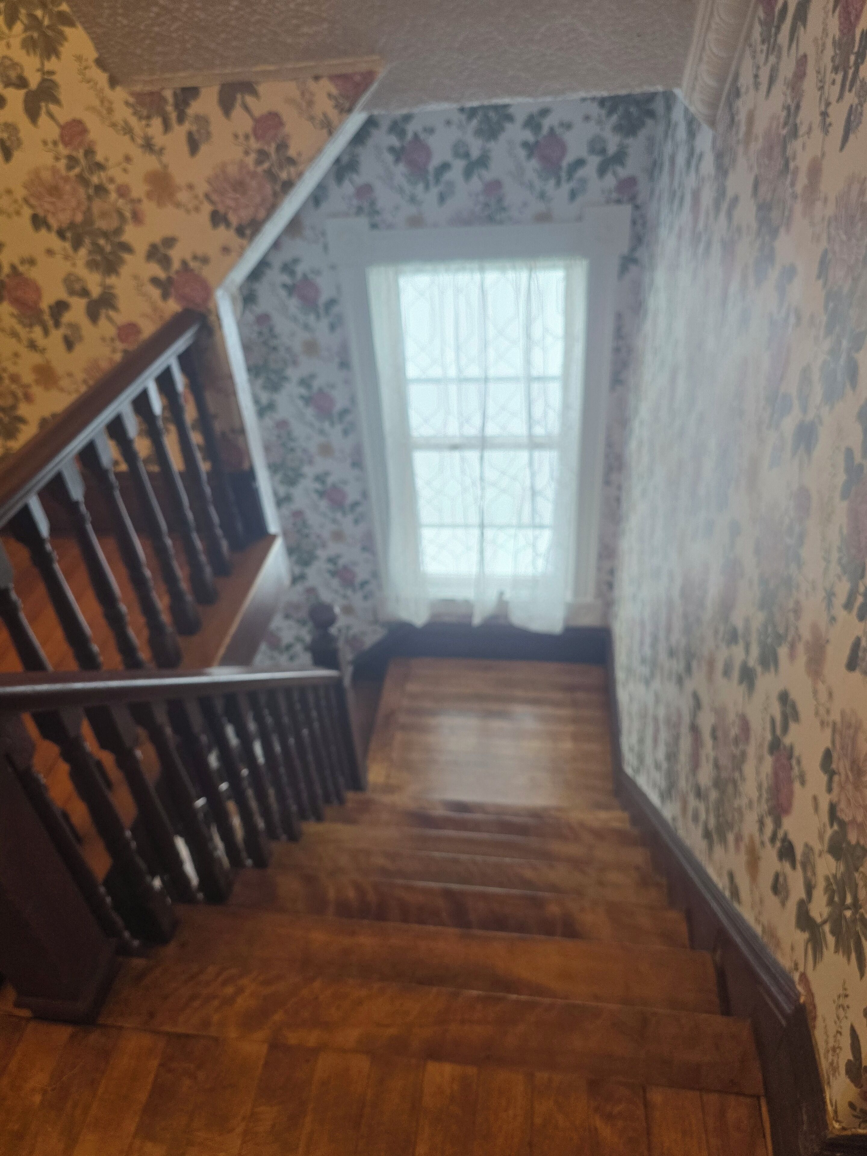 Un escalier en bois avec une rampe, menant à un palier doté d’une fenêtre.