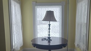 A room with a round table, a lamp, and a window with curtains. - Keepsake Inn - Where Memories are Made (Colebrook)