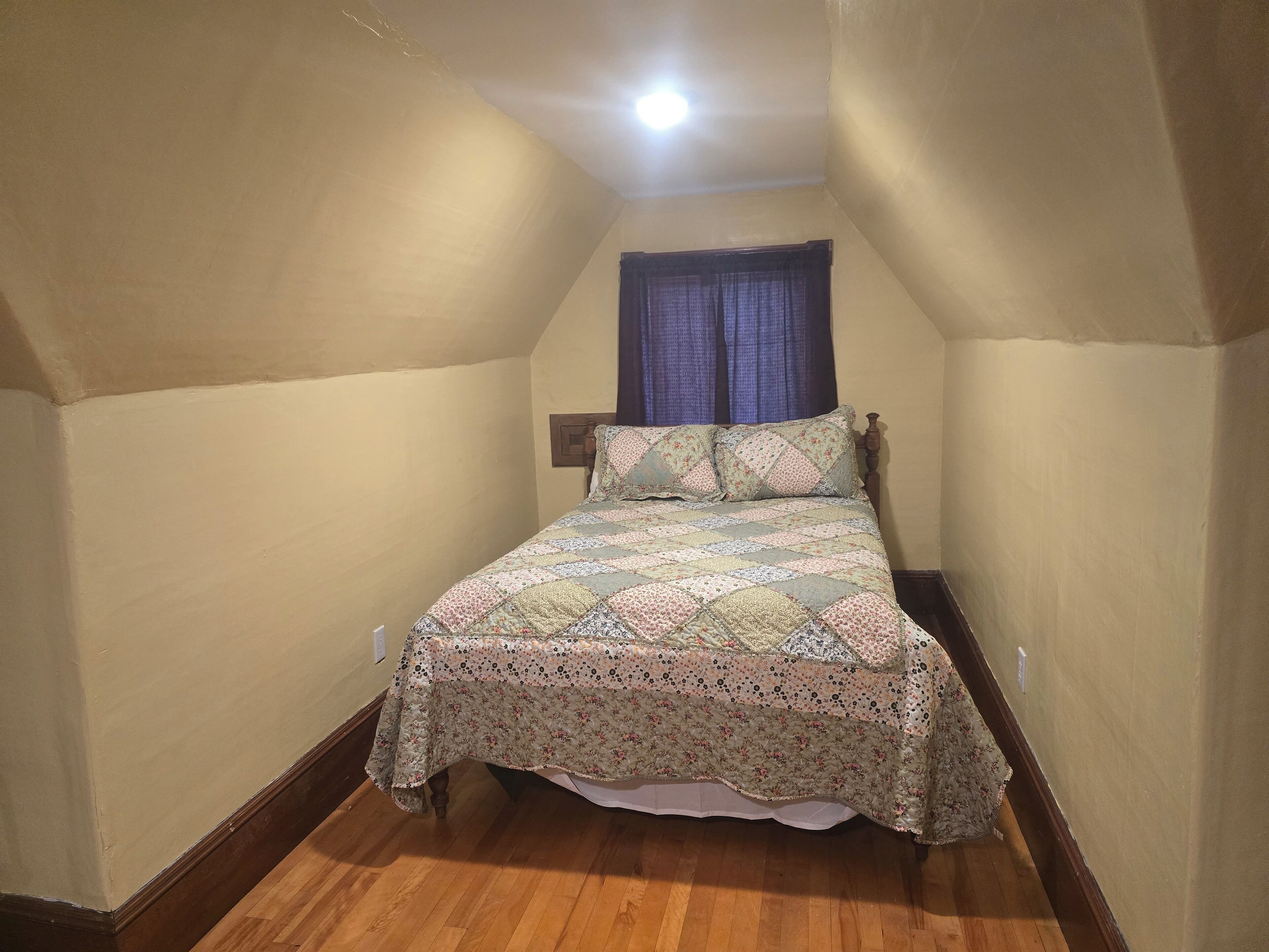 Quarto com cama, piso de madeira e teto inclinado.