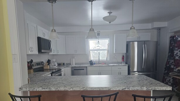 A kitchen with white cabinets, a granite countertop, a stainless steel refrigerator, and a window with a view of trees. - Keepsake Inn - Where Memories are Made (Colebrook)