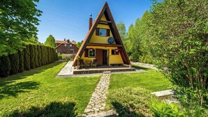 Una casa de forma triangular con un camino de piedra que lleva a la entrada, rodeada de un césped cuidado y setos.