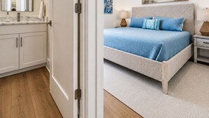 Una camera da letto con un letto, comodini, una ventola a soffitto, un quadro e un bagno con uno specchio e mobiletti.