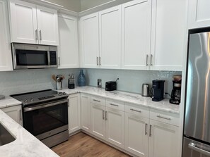 A modern kitchen with white cabinets, stainless steel appliances, and a marble countertop. - Newer Luxury 4-bedroom 4-bath cottage with community pool 2 minute walk to beach (Gulf Shores)