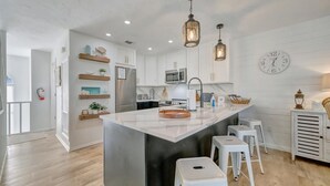 Une cuisine moderne avec des meubles blancs, un îlot central doté de tabourets, un éclairage suspendu et une horloge au mur.