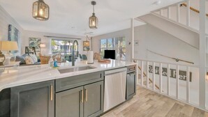 Une cuisine moderne dotée d’un îlot central, de luminaires suspendus et d’un escalier avec une rampe.