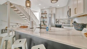 Une cuisine moderne dotée d’un îlot central, d’appareils électroménagers en acier inoxydable et de luminaires suspendus.