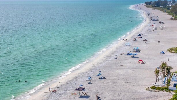 Une plage avec des tentes et des parasols, un rivage sablonneux et l’océan.