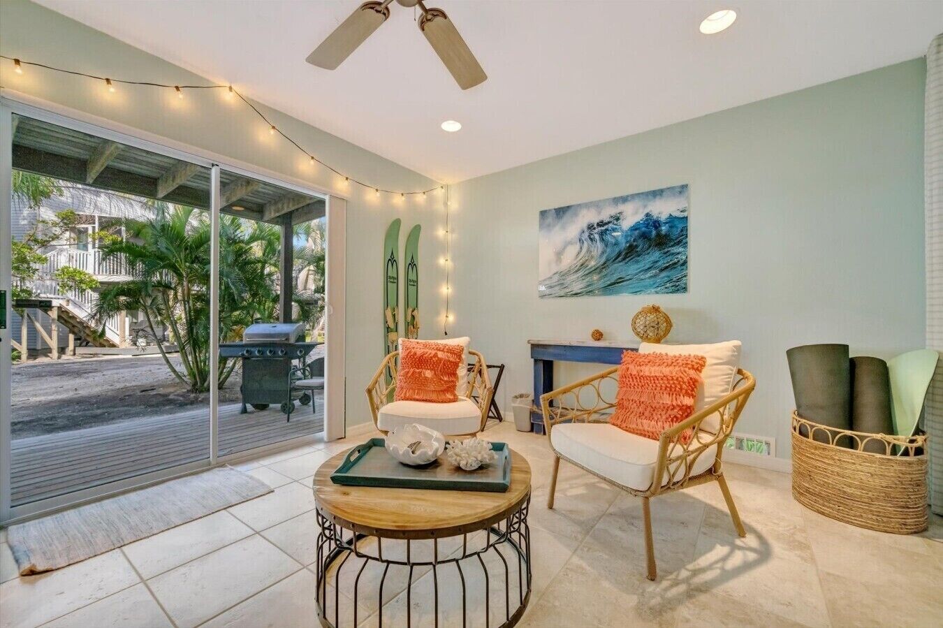 A room with a glass door leading to a balcony, wicker chairs, a round table, and a painting on the wall.