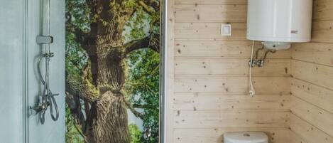 A bathroom with a wooden wall, a toilet, a shower, and a large tree mural.