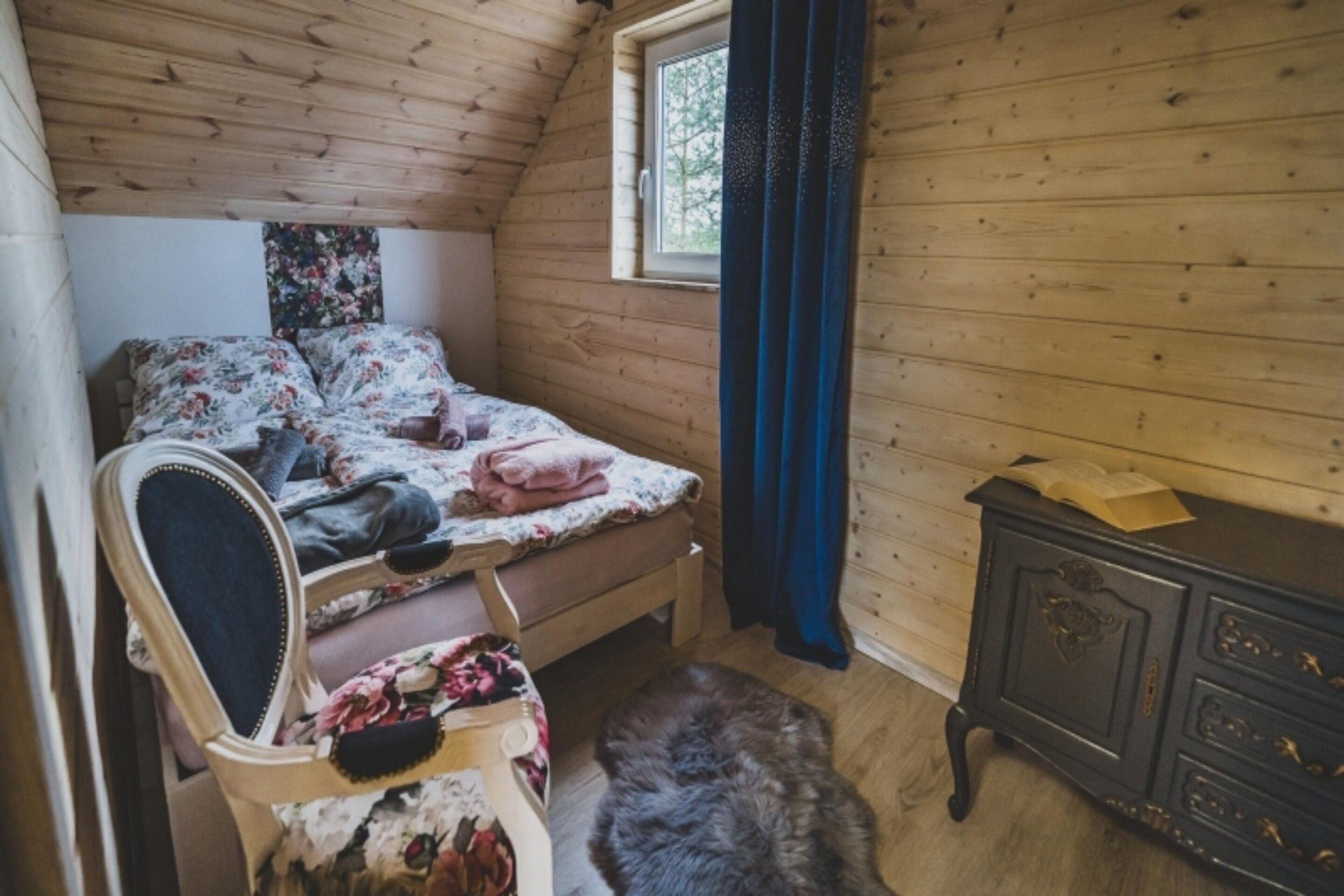 A bedroom with a wooden ceiling, a bed with floral bedding, a dresser, and a window with curtains.