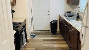 A kitchen with wooden cabinets, a stainless steel sink, and a black trash bin.