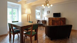 Un comedor con una mesa y sillas de madera, un televisor en un mueble y una araña.