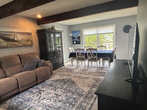 A living room with a sofa, a cabinet, a dining table with chairs, a rug, and a TV stand. - Waterfront River House on Brices Creek, New Bern (New Bern)