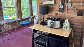 A rustic kitchen with a crockpot, a table, chairs, and a view of greenery outside. - Waterfront River House on Brices Creek, New Bern (New Bern)