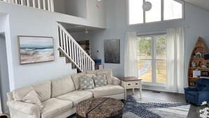 A spacious living room with a beige sectional sofa, a round coffee table, and a large window with curtains. - Waterfront River House on Brices Creek, New Bern (New Bern)