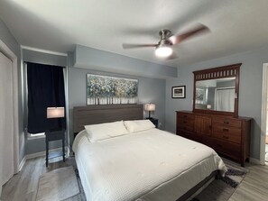 A bedroom with a bed, a dresser, a ceiling fan, a painting, and a window with curtains. - Waterfront River House on Brices Creek, New Bern (New Bern)