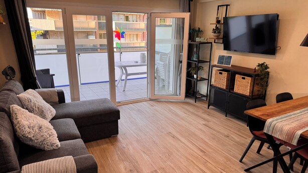 Ein modernes Wohnzimmer mit Sofa, Esstisch, Fernseher und einer Glastür, die zu einem Außenbereich führt.