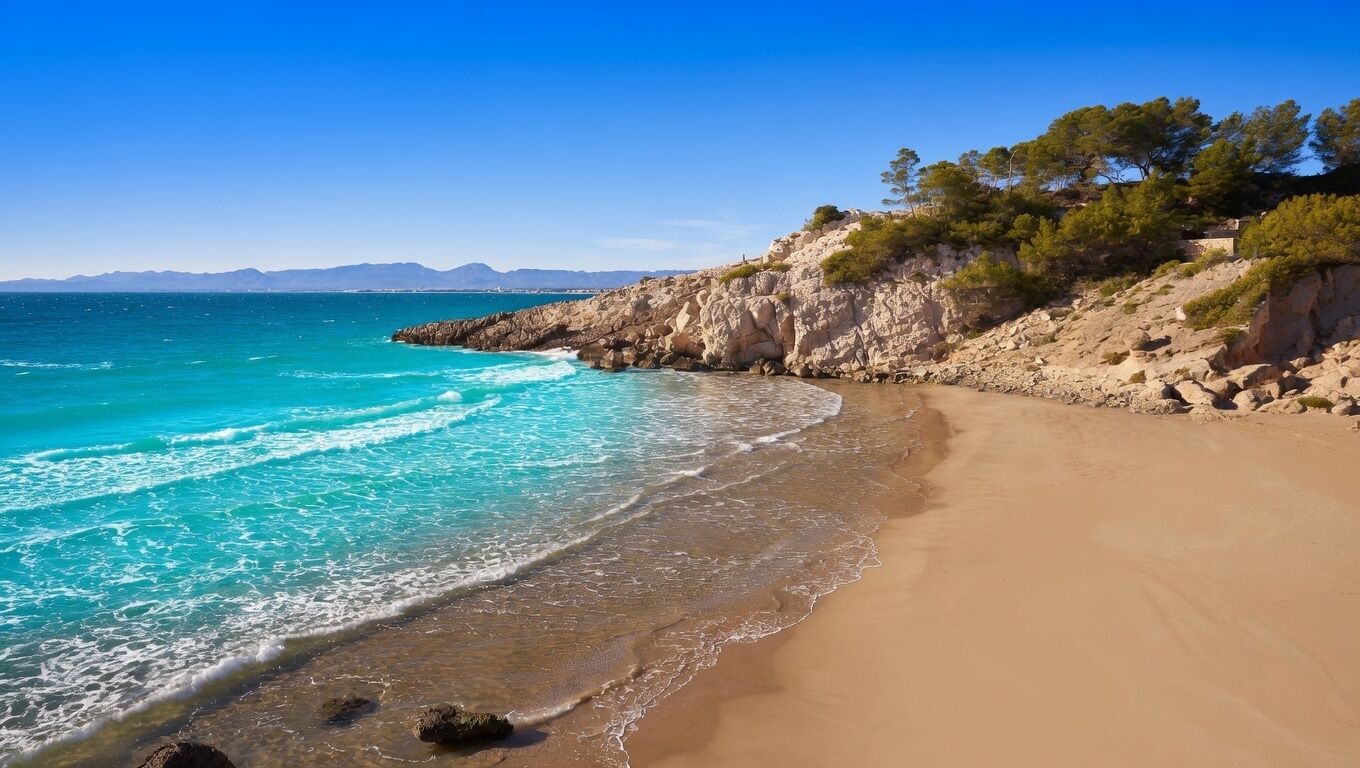 A beach with clear turquoise waters, a sandy shore, and rocky cliffs with sparse vegetation.