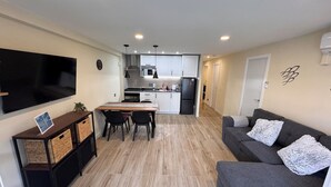 A modern living room with a flat-screen TV, a gray sofa with fluffy pillows, a wooden dining table with chairs, and a kitchen in the background. - Casa Márquez - Beach apartment in the Golden Coast (Salou)