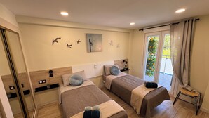 Ein Hotelzimmer mit zwei Betten, einer Dusche, einem Balkon mit Pflanzen und einem Gemälde an der Wand.