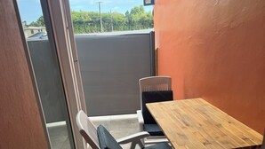 En lille balkon med et træbord og to stole, hvoraf den ene har en sort pude.