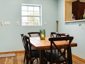 A dining area with a wooden table and chairs, a window, and a wall-mounted shelf with a plant. - Tropical Pool Retreat + Walk to River + Pet Friendly (Fort Pierce)