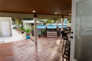 Ein überdachter Patio-Bereich mit Pool, Holzterrasse und Gartenmöbeln.