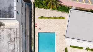 Vista aérea de um edifício com piscina, área de estacionamento e vegetação.