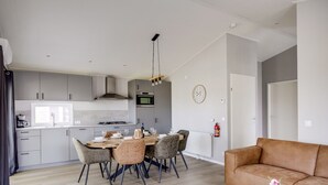 A modern kitchen with a dining area, a sofa, and a small table with a vase. - Villa Riant 63 | 6 persoons vakantiehuis (Zennewijnen)