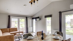 A dining area with a wooden table set for four, a sofa, and a view of the outdoors. - Villa Riant 63 | 6 persoons vakantiehuis (Zennewijnen)