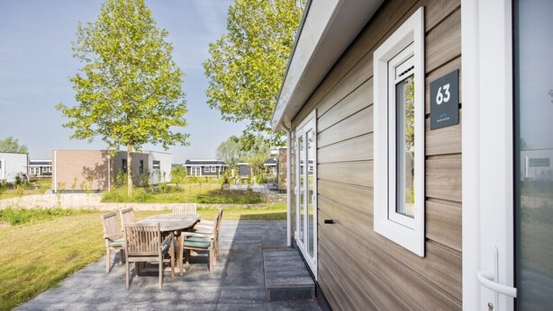 A modern mobile home with a patio area, a dining table, and chairs. - Villa Riant 63 | 6 persoons vakantiehuis (Zennewijnen)