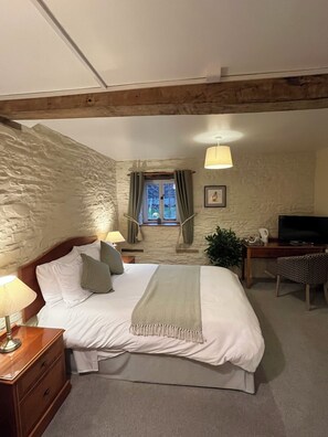 A bedroom with a bed, bedside table, lamp, window with curtains, a desk with a chair, a television, and a plant. - The Bateman Arms (Shobdon)