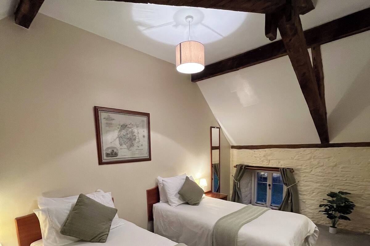 A room with two beds, a ceiling fan, a framed map on the wall, and a window with curtains.