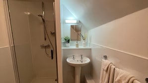 A modern bathroom with a glass shower enclosure, a pedestal sink, and a bathtub with towels. - The Bateman Arms (Shobdon)