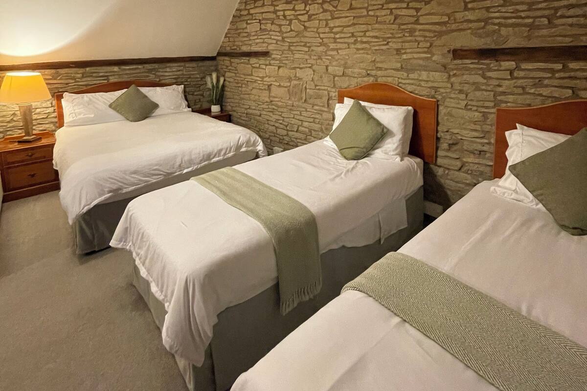 A room with three beds, a stone wall, and a sloped ceiling.
