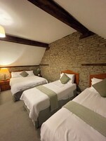 Una habitación con tres camas, una pared de piedra y techo inclinado.