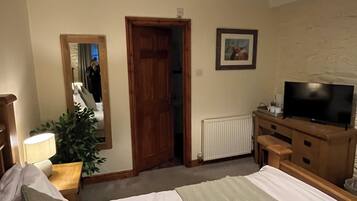 A hotel room with a large bed, a television, a wooden dresser, a mirror, and a radiator.