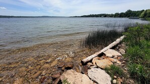Ein See mit klarem Wasser, einer steinigen Uferlinie und einer entfernten Baumgrenze.