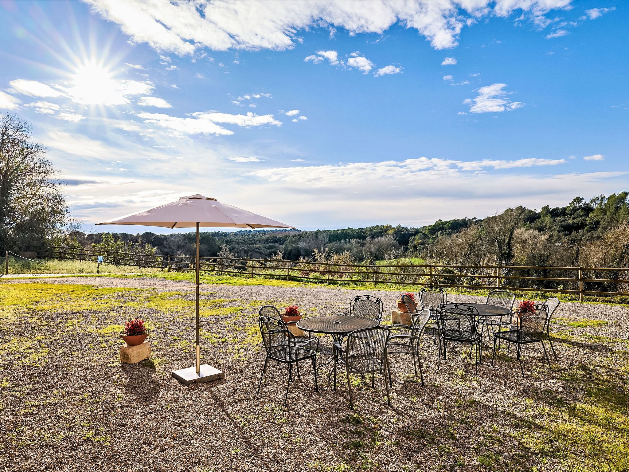Un espace extérieur aménagé pour les repas, avec une table et des chaises, un grand parasol et un sol recouvert de gravier.