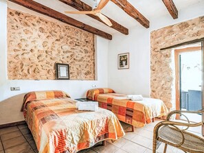 Quarto com duas camas, ventoinha no teto, paredes de pedra e uma janela.