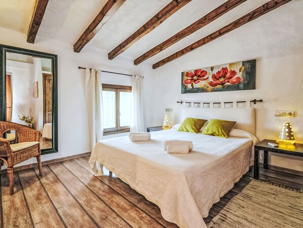 Une chambre à coucher avec un grand lit, un plancher en bois, un tableau représentant des fleurs et une table de chevet avec une lampe.