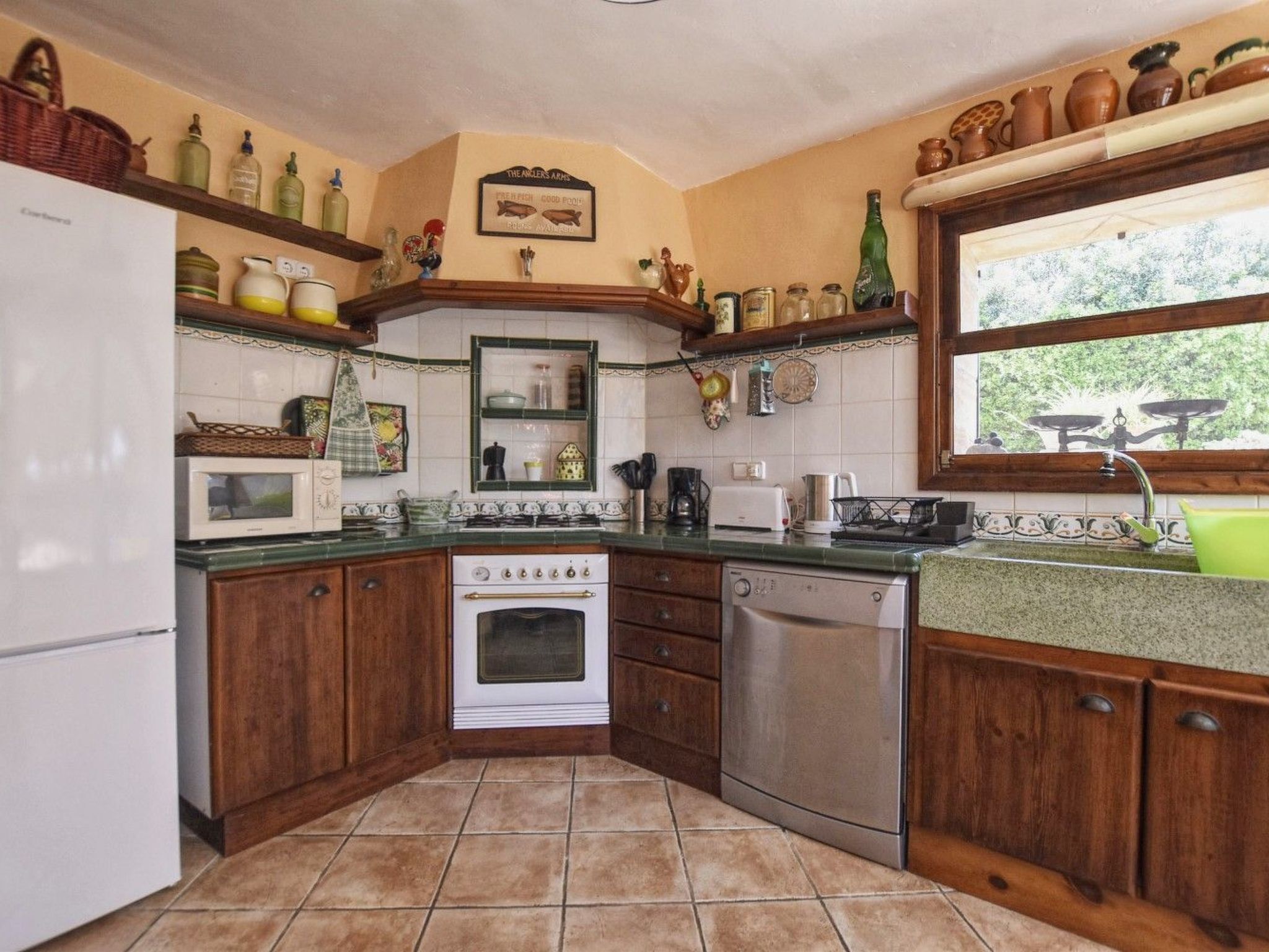 A kitchen with wooden cabinets, a stove, a microwave, and a dishwasher. There are shelves with various kitchen items and a window with a view of greenery.