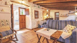 A rustic living room with exposed wooden beams, a striped sofa, a rocking chair, and a small table with a book and remote control. - MONTSERRAT  ( SON PERETO ) by Interhome (Manacor)
