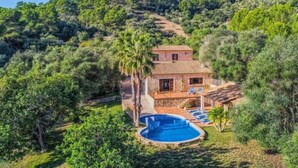Uma casa de dois andares com piscina, cercada por vegetação exuberante e colinas.