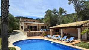 Piscina com espreguiçadeiras, um edifício de pedra e um espaço de pátio coberto.