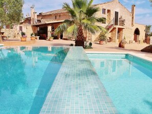 A swimming pool with tiled edges, surrounded by stone buildings with balconies and potted plants. - Finca "Son Gabriela" mit eigener Terrasse by Interhome (Llucmajor)