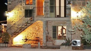 Ein Steinhaus mit einer Treppe, die zu einem Balkon führt, Außenbeleuchtung und einem Blumentopf.