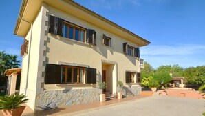 Une maison à deux étages, avec des fondations en pierre, de nombreuses fenêtres dotées de volets et une allée pavée.